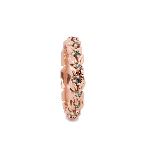 A rose gold eternity ring featuring a detailed floral pattern with small green gemstone accents, shown on a plain white background.